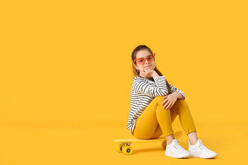 Fototapeta premium Cute little girl with skateboard on color background