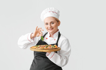 Mature female chef with tasty pizza on grey background