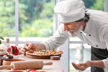 Mature male chef with tasty pizza in kitchen