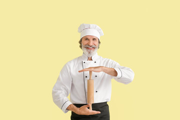 Mature male chef with rolling pin on color background