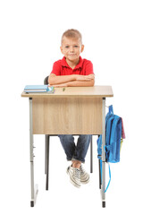 Little pupil sitting at school desk against white background