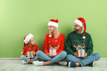 Young family with Christmas gifts sitting on floor near color wall