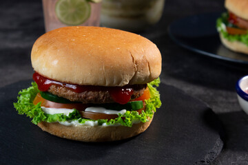 Delicious fresh meat burgers with tomato sauce and vegetables on a dark background.
