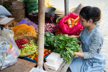 Asian woman greengrocer arranges spinach for her vegetable stall display at a traditional market