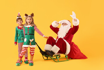 Cute little elves with Santa Claus sitting on sledge against color background