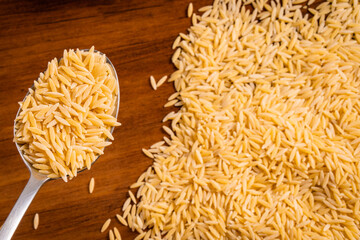 Raw dry uncooked Orza Risoni pasta spaghetti noodle on white bowl wooden background for basil tomato pesto sauce Homemade Italian food organic whole wheat vegan spaghetti for a healthy meal