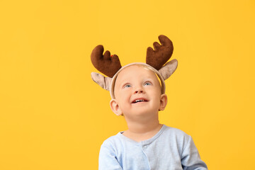 Cute little baby with deer horns on color background