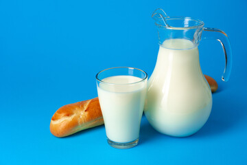 Fresh baguette bread and pitcher with fresh milk on blue background
