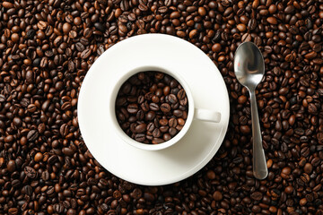 Cup and spoon on coffee beans background, top view