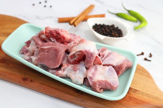 Fresh raw goat meat or mutton or lamb pieces. Preparation for Indian mutton curry. Spice at the background such as cinnamon sticks, red chili powder, black pepper & coriander. Copy space.