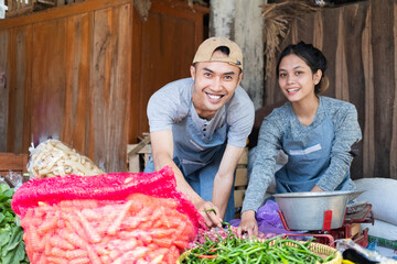 greengrocer couple smiles as they put together a vegetable display at a vegetable stall at a traditional market