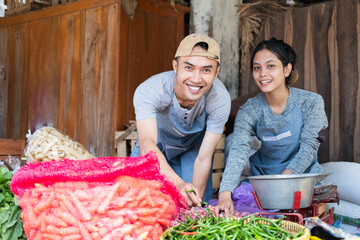 greengrocer couple smiles as they put together a vegetable display at a vegetable stall at a...
