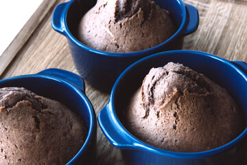 Delicious baked chocolate muffins in blue ceramic tins on wooden background. Side view