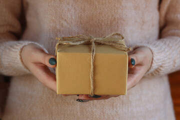 Female hands hold a gift wrapped in kraft paper. Zero waste concept