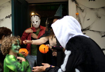 Fototapeta premium Hosts giving candies to a group of trick-or-treating kids during Halloween