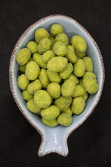 crunchy peanuts coated with wasabi ready for finger food served in a light blue bowl on a black background
