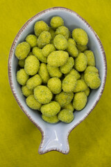 crunchy peanuts coated with wasabi ready for finger food served in a light blue bowl on a yellow background
