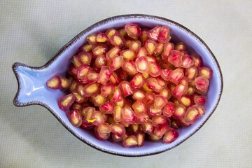 evocative image of pomegranate grains ready for healthy finger food served in a light 
blue bowl on a white background