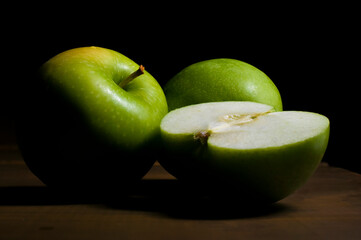 still life, Green apple half and green apples with a chiaroscuro, baroque style with black background on a wooden vintage table 
