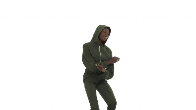 Exited African woman wearing in hooded tracksuit dancing in afro style. Dancer stepping side-to-side, shuffle, pushing knees in and out, raising hands in course. Isolated on white background.