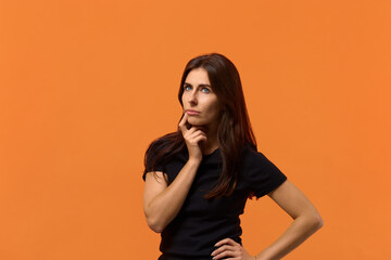 What to give him. Thoughtful caucasian woman in black t-shirt keeps fore finger near lips, being...