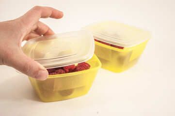 A woman's hand closes the lunchbox, the photo shows a hand and two yellow lunchboxes with raspberries