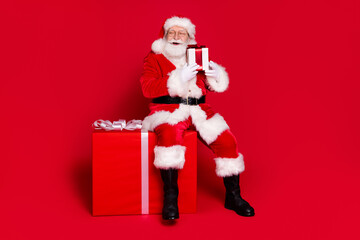 Full length body size view of his he handsome fat overweight cheerful Santa sit on large big giftbox event festal occasion newyear isolated bright vivid shine vibrant red color background