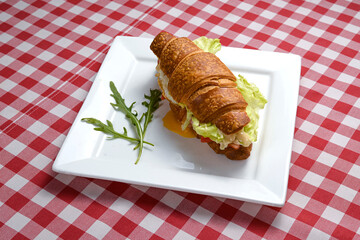 Savory croissant with tomato, letuce and cheese served on a white plate over over red plaid tablecloth.