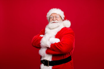 Photo of retired grandpa grey beard crossed hands self-assured smile wait elves prepare deer trip wear x-mas costume white gloves coat spectacles headwear isolated red color background
