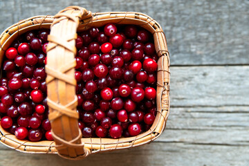Red cranberries in a wicker basket on a wooden rustic background.
