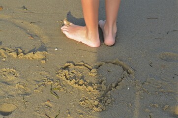 Drawing of a heart in the sand and a child feet standing behind