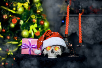 Human skull with evil glowing eyes in a Christmas hat lies in fog on a table next to smoking...