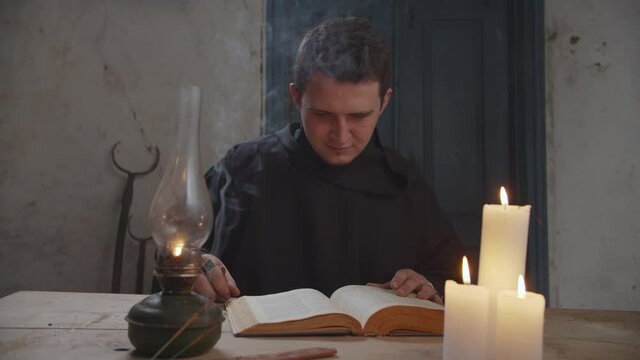 Concentrated mysterious wizard in black robe foretelling future, reading vintage spellbook, casting magic rune stones to interpret vision and fate while practicing divination in rustic house.