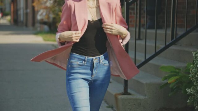 Petite Woman With Her Tight Jeans And Pink Suit Walking On The Sidewalk During Daytime. - Tilt-Up Full Body Shot