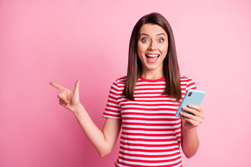 Photo portrait of amazed woman keeping cellphone pointing with finger at copyspace isolated on pastel pink color background