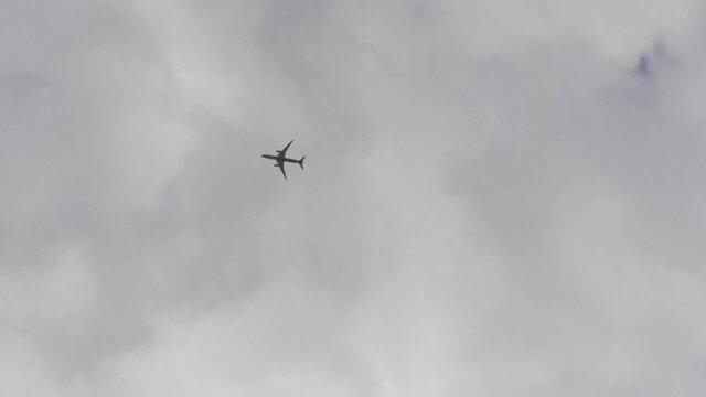 Vertical video of looking up to the sky as an airplane flies by. Pov flying silhouetted plane on cloudy day. Wide angle shot