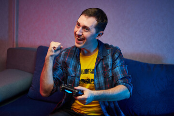 Portrait of crazy playful Gamer, boy enjoying Playing Video Games indoors sitting on the sofa, holding Console Gamepad in hands. Resting At Home, have a great Weekend