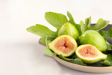 Brown plate of whole figs and halved with fig leaves and white background.