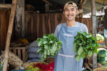 Smiling Asian man selling vegetable stall brings mustard greens against the vegetable stand in the...