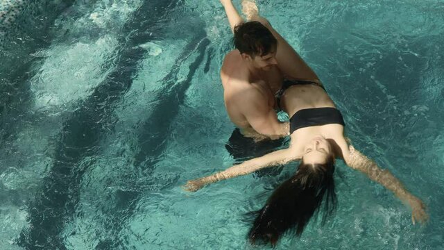 Handsome man carrying beautiful woman in arms in pool. Couple relaxing in spa.