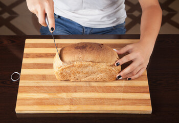 Young woman cutting bread with knife.