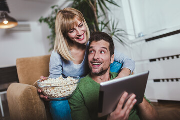 Young couple watching media content online in a tablet in the living room.