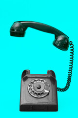 A vintage landline telephone with raised handset on an aqua blue background. Retro style dial phone.