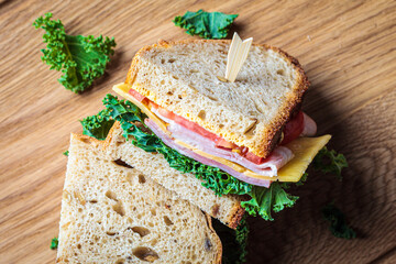 Sandwiches with ham, cheese, vegetables and kale on a wooden board, top view.