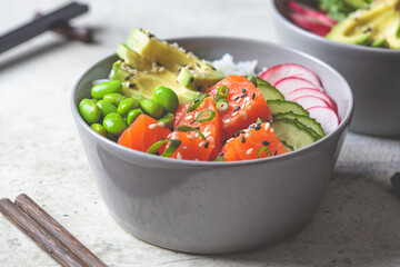 Poke bowl with salmon, rice, avocado, edamame beans, cucumber and radish in gray bowl. Hawaiian ahi poke bowl, gray background.