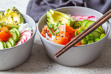 Poke bowl with salmon, rice, avocado, edamame beans, cucumber and radish in gray bowls. Hawaiian ahi poke bowl, gray background.