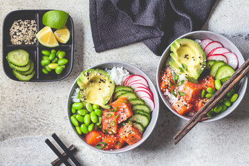 Poke bowl with salmon, rice, avocado, edamame beans, cucumber and radish in a gray bowls, top view....