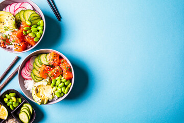 Poke bowl with salmon, rice, avocado, edamame beans, cucumber and radish in gray bowls, top view....