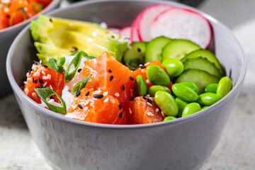 Poke bowl with salmon, rice, avocado, edamame beans, cucumber and radish in gray bowl. Hawaiian ahi poke bowl, gray background.
