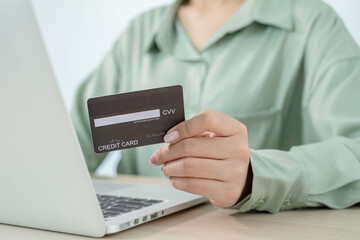 The businesswoman's hand is holding a credit card and using a laptop for online shopping and internet payment in the office